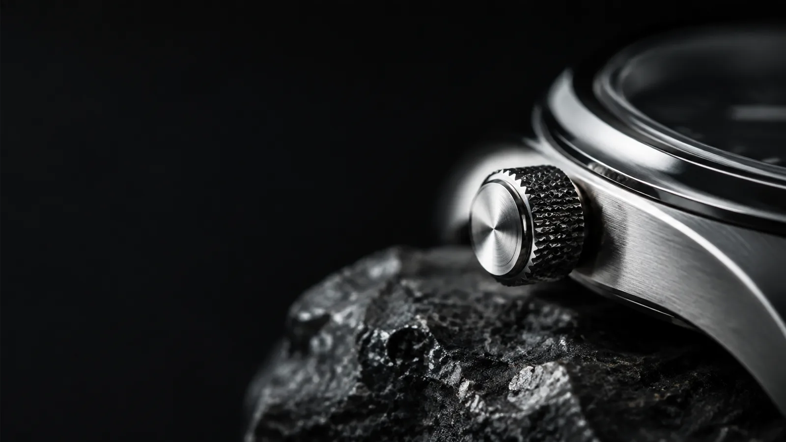 Extreme close-up of a machined silver watch crown against dark mineral stone